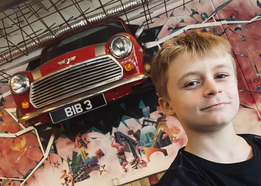 A child smiling in front of a Mini car art installation at Birmingham's Baked in Brick restaurant