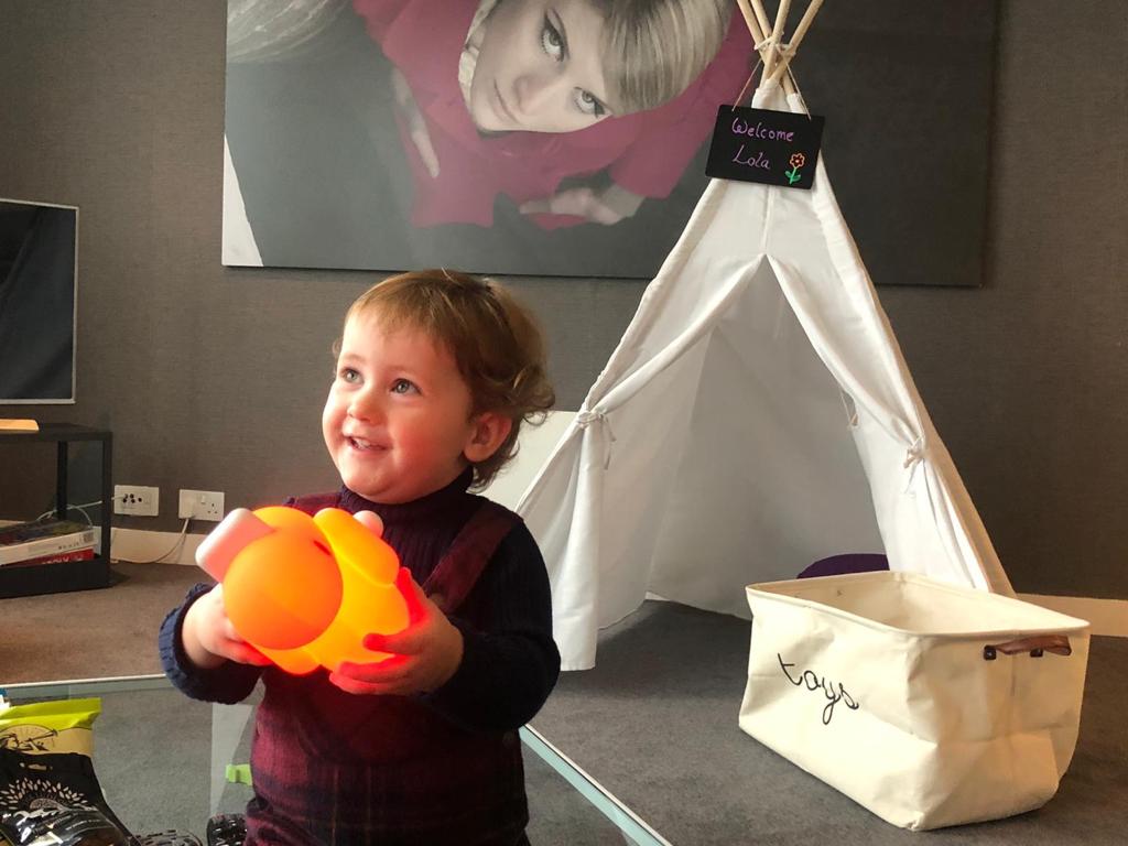 Eco tourism. Toddler smiling whilst enjoying playing with a toy duck and a little tipi in an apartment at Staying Cool at the Rotunda