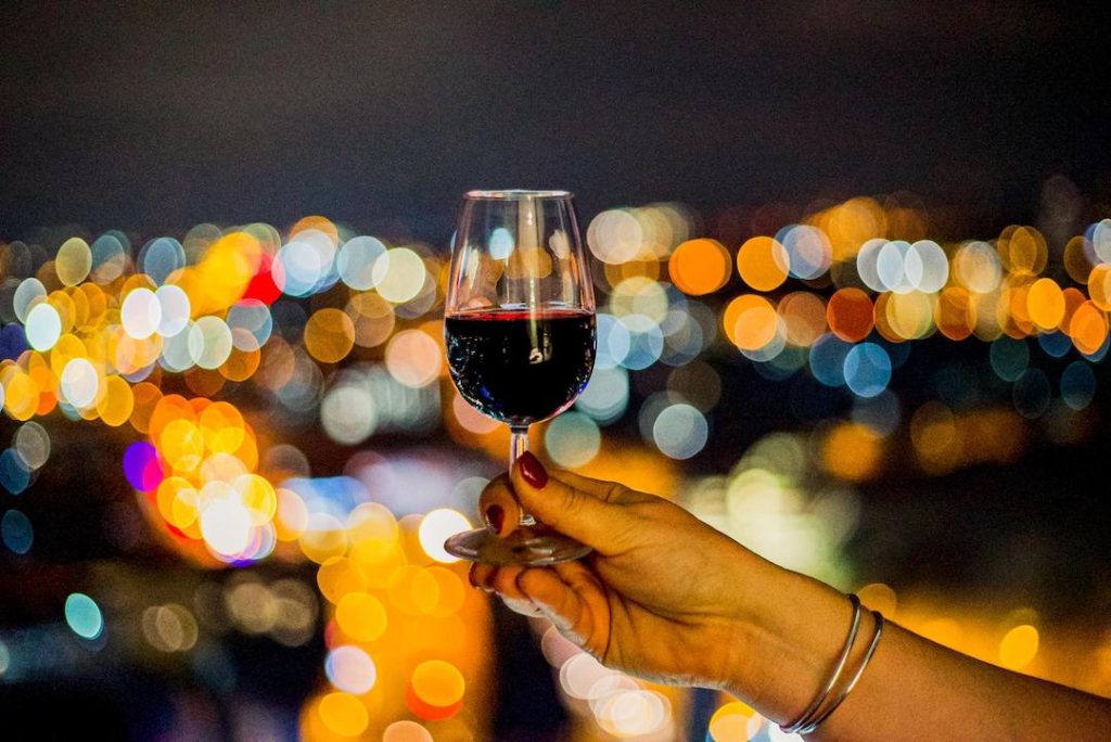 Glass of red wine with city lights in the background at night at Staying Cool's Rotunda Aparthotel