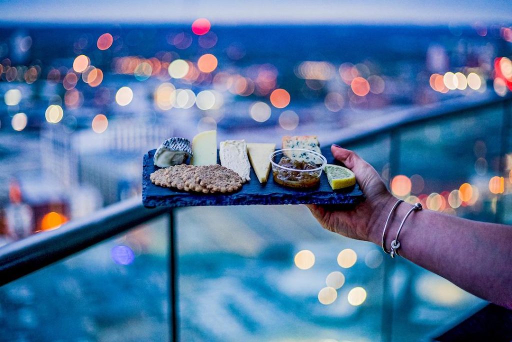 Cheese board selection with city lights in the background at Staying Cool's Rotunda Aparthotel