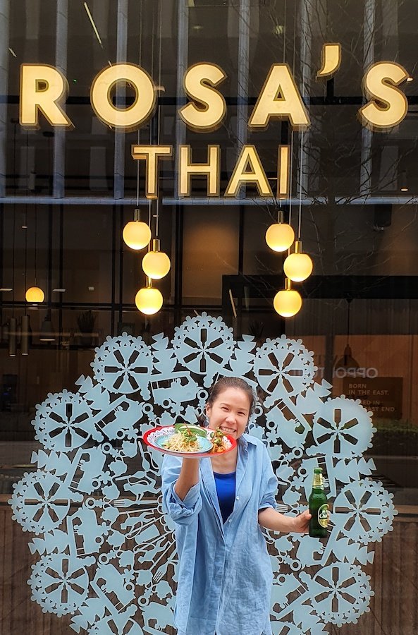 A member of the Rosa's Thai Cafe team standing outside one of their beautiful venues with thai food and a beer in hand.