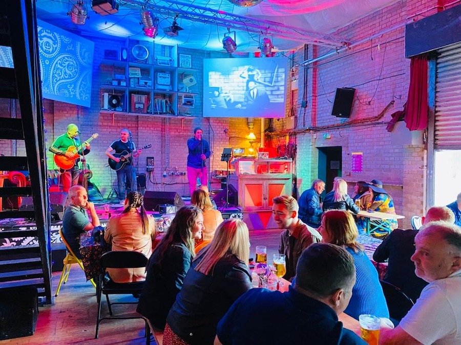 A band performing on stage inside The Night Owl, an independent live music venue.